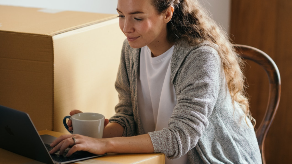 Une femme sur son pc portable et des cartons de déménagement